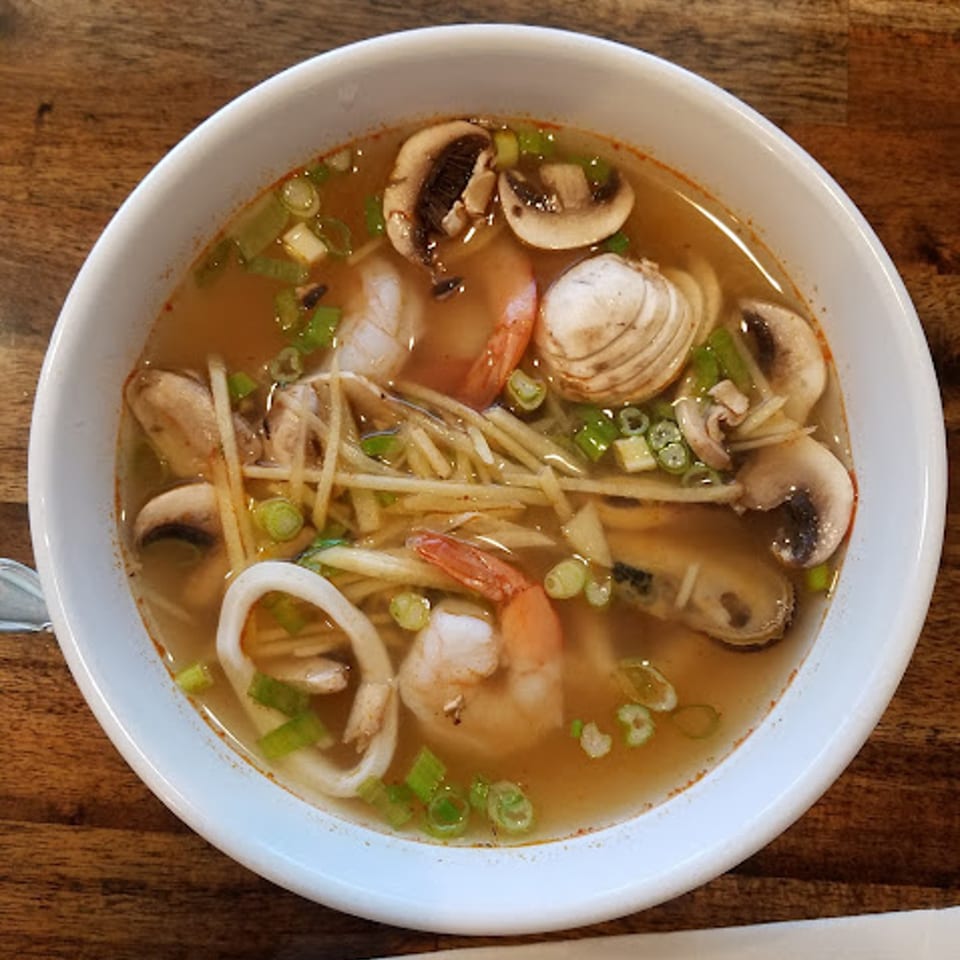 A bowl of Thai Tom Yum soup with shrimp, squid, mussels, clams, mushrooms, and scallions.